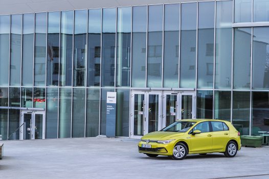 Gul Volkswagen Golf framför glasfasad