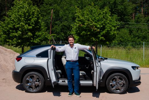 En vit Mazda MX-30 med tillhörande testpilot i värmen.