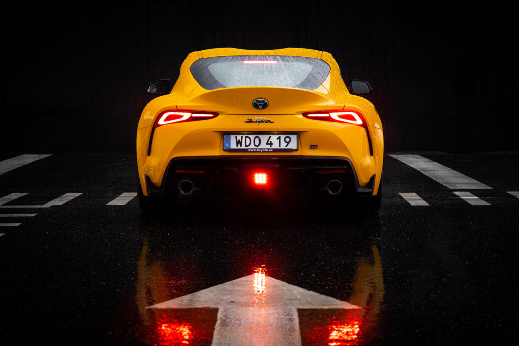 Gul Toyota GR Supra bakifrån som reflekteras i regnet